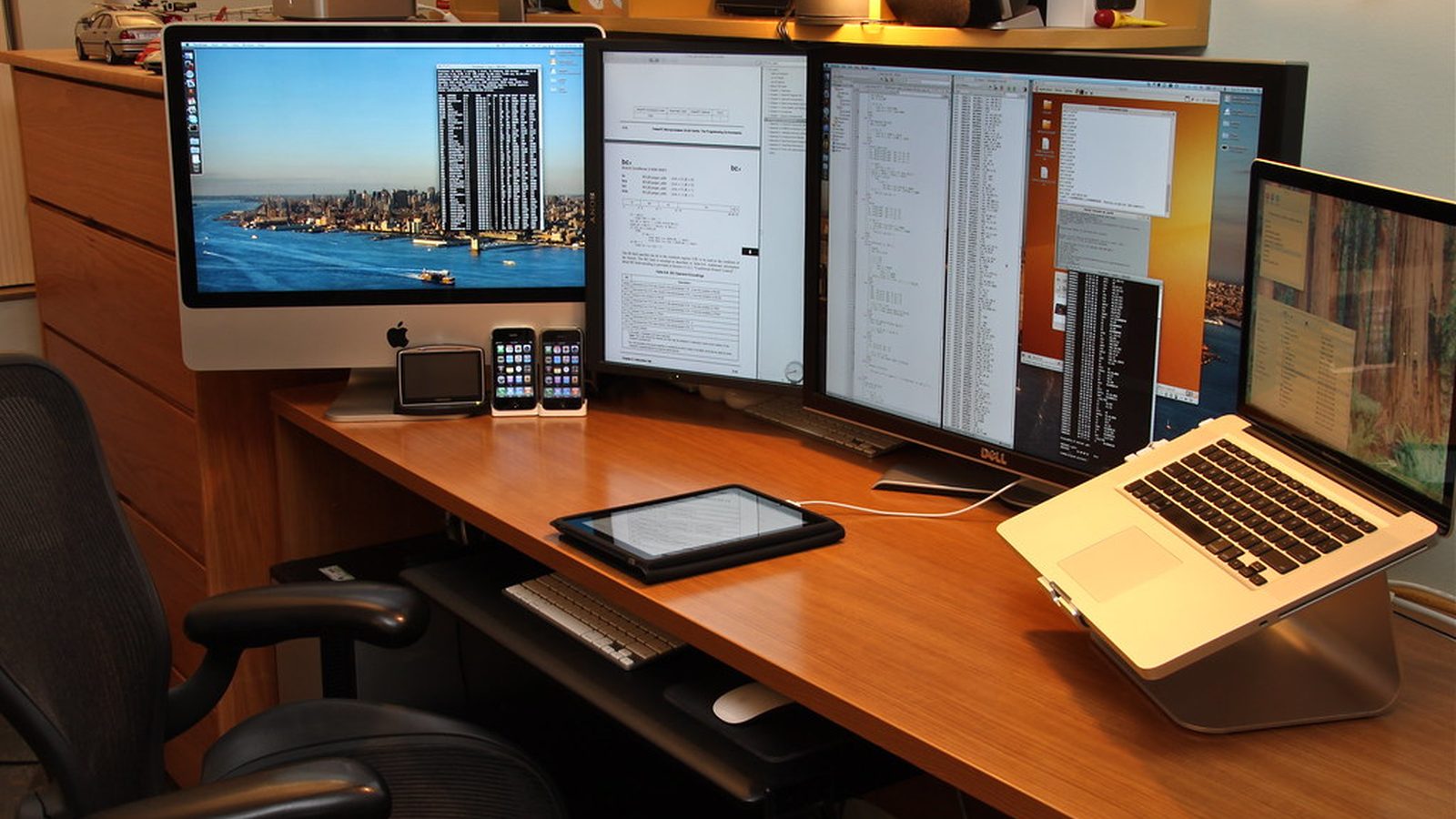 A desk with several monitors, a laptop, a tablet and two phones